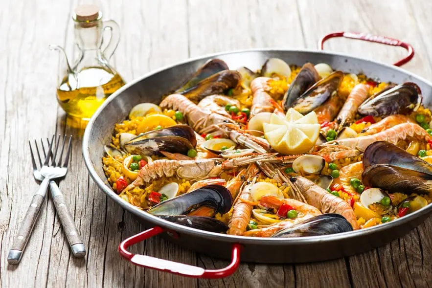 La imagen representa una exquisita paella de mariscos, un plato emblemático de la cocina mediterránea. Con gambas, mejillones, almejas y verduras frescas, la paella destaca por sus colores vibrantes y su sabor auténtico. Preparada con arroz de calidad y aceite de oliva, es perfecta para compartir en reuniones familiares o eventos, siendo un símbolo de la gastronomía tradicional catalana y española.