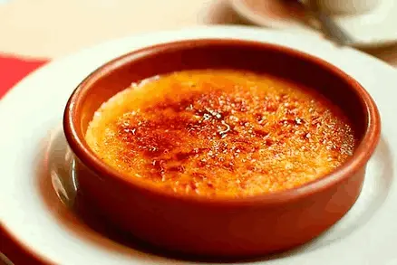 La imagen muestra la crema catalana, un postre tradicional y emblemático de Cataluña. Elaborada con yema de huevo, azúcar, leche y un toque de canela y limón, su característica capa caramelizada aporta un contraste de texturas único. Este delicioso manjar es ideal para los amantes de los postres tradicionales, siendo un símbolo indiscutible de la repostería catalana.