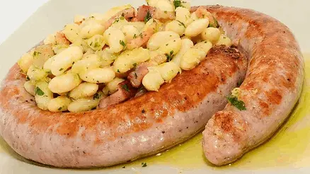 La imagen muestra un plato típico de la gastronomía catalana: butifarra con mongetes. Este delicioso manjar combina la jugosidad de la butifarra, un embutido tradicional, con la suavidad y el sabor de las judías blancas salteadas. Un plato sencillo pero lleno de tradición, ideal para disfrutar en cualquier época del año y perfecto para los amantes de la cocina auténtica de Cataluña.