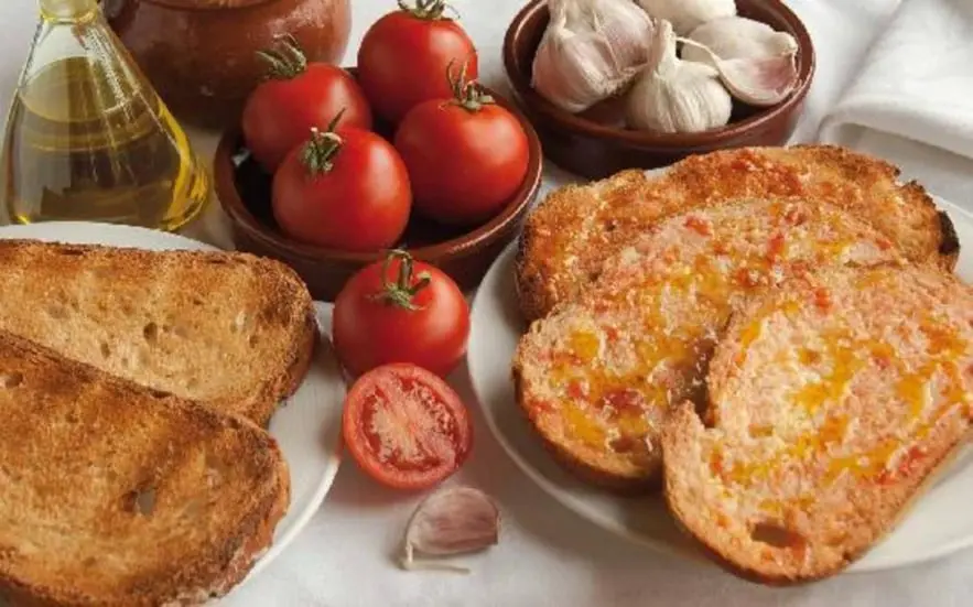 Esta imagen representa el icónico pan con tomate, un símbolo de la gastronomía catalana. Con pan tostado, tomate fresco, aceite de oliva virgen extra y ajo, es un ejemplo de la dieta mediterránea saludable. Ideal como aperitivo o acompañamiento, este plato tradicional catalán destaca por su sencillez y autenticidad, siendo una joya culinaria reconocida en todo el mundo.