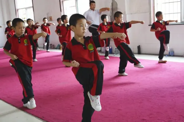 Niños practicando artes marciales en una clase de kung-fu en China, mostrando disciplina y técnica bajo la guía de un instructor. La imagen resalta la importancia del entrenamiento desde temprana edad, fomentando valores como la concentración, el respeto y la fortaleza física. Ideal para contenido relacionado con la enseñanza de kung-fu, el desarrollo infantil a través de las artes marciales y la cultura deportiva en China.