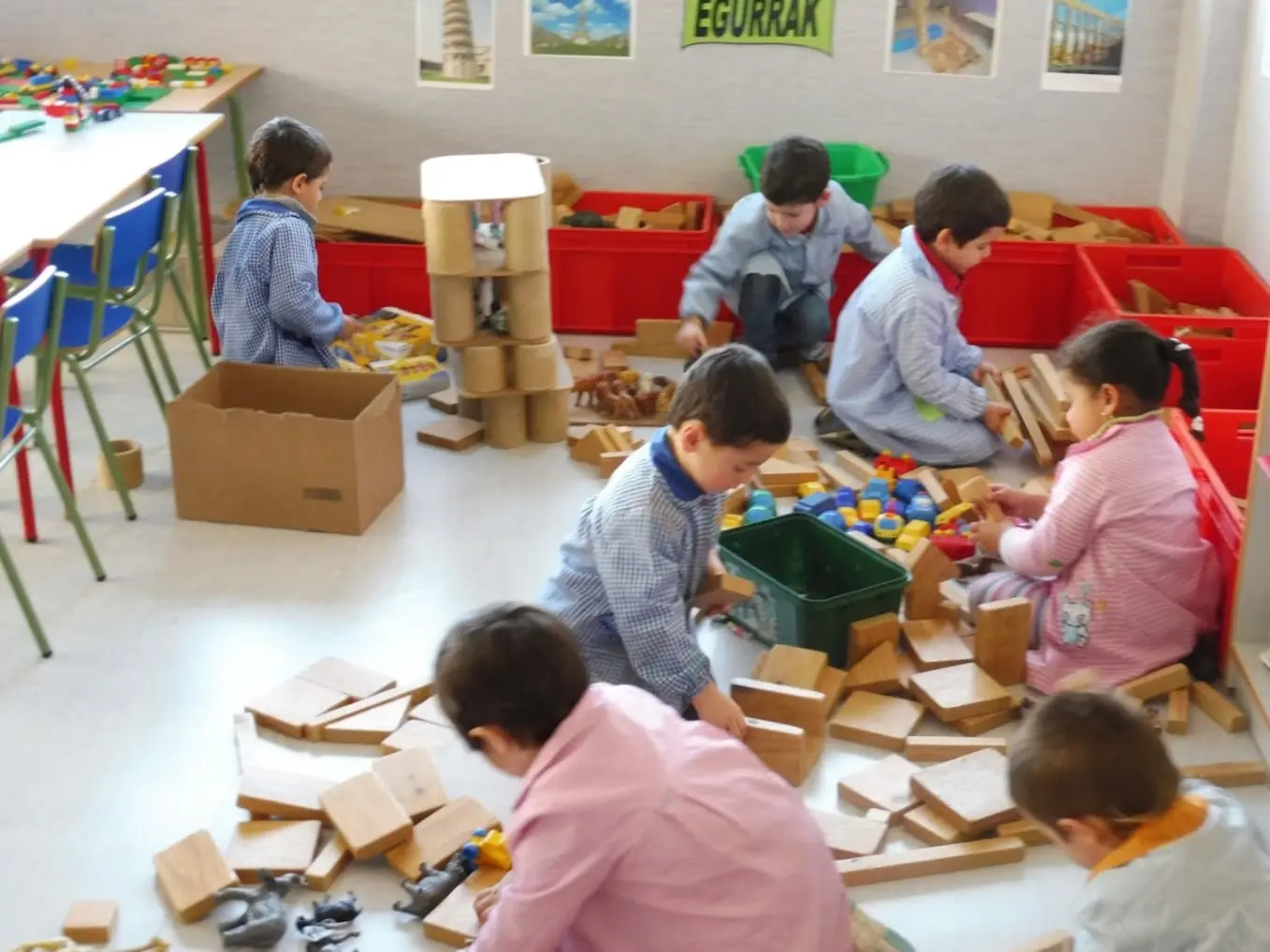 "Aula de educación infantil donde niños juegan y construyen con bloques de madera y materiales didácticos. Un espacio diseñado para fomentar la creatividad, el trabajo en equipo y las habilidades motoras. Ideal para actividades de aprendizaje práctico y desarrollo cognitivo temprano. Un entorno educativo dinámico que promueve la exploración y el aprendizaje a través del juego.