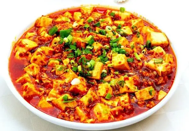 Exquisito Mapo Tofu, un icónico plato de la cocina de Sichuan. Este manjar combina tofu suave con una salsa picante a base de doubanjiang (pasta de frijol y chile), carne molida y aromáticos cebollines. Su sabor intenso y especiado es un deleite para los amantes de la comida china tradicional, destacando por su toque audaz y suculento.