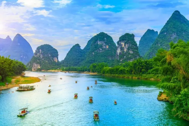 La imagen muestra el río Li en Guilin, China, rodeado de montañas kársticas y exuberante vegetación. Barcas recorren las aguas cristalinas, ofreciendo un paisaje sereno y espectacular. Este destino es perfecto para quienes buscan belleza natural y experiencias culturales únicas. Reconocido por su impacto visual, el río Li es un lugar icónico y esencial en el turismo chino.