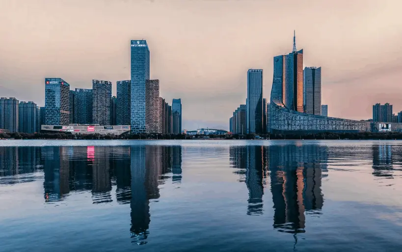 La imagen muestra el horizonte moderno de Hefei, con rascacielos imponentes reflejándose en las tranquilas aguas de un lago. La arquitectura contemporánea contrasta con el cielo al atardecer, creando una escena vibrante y elegante. Este paisaje urbano refleja el rápido desarrollo y la importancia económica de Hefei, consolidándose como un centro tecnológico y cultural en China.