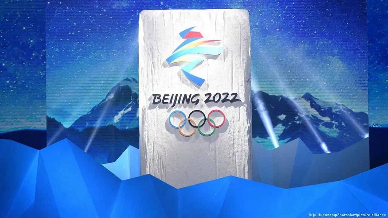 La imagen muestra el logotipo oficial de los Juegos Olímpicos de Invierno de Beijing 2022 en un escenario decorado con motivos invernales y montañas estilizadas. Estos juegos marcaron un hito, ya que Beijing se convirtió en la primera ciudad en albergar tanto los Juegos Olímpicos de Verano (2008) como los de Invierno. La imagen resalta el espíritu olímpico y la belleza del deporte en la temporada invernal. Los anillos olímpicos y el logotipo colorido enfatizan la celebración global del deporte y el compromiso de China con los eventos internacionales de gran escala. El fondo montañoso representa los deportes de invierno y el entorno natural en el que se llevaron a cabo muchas de las competiciones.