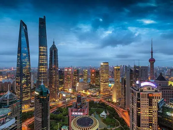 Esta imagen muestra el impresionante horizonte de Shanghái durante la noche, destacando la moderna área de Pudong con sus famosos rascacielos. Entre las edificaciones visibles se encuentran la Torre de Shanghái, el Shanghai World Financial Center y la Torre de la Perla Oriental, los cuales forman parte de uno de los paisajes urbanos más icónicos y futuristas de China. La imagen captura la vibrante vida nocturna de la ciudad, con edificios iluminados y un dinámico entramado de avenidas. Shanghái, como la capital económica de China, representa la fusión de modernidad y tradición, y se ha convertido en un importante atractivo turístico para viajeros interesados en la arquitectura contemporánea y la innovación tecnológica.