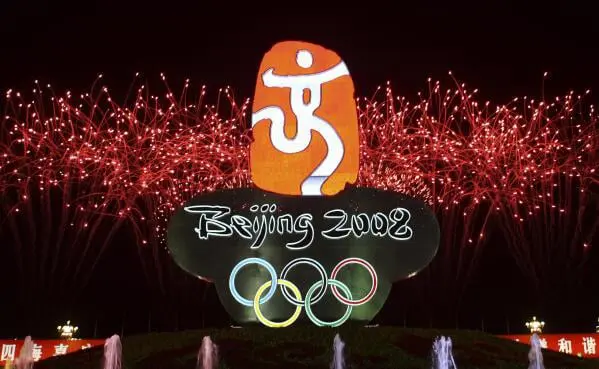 La imagen muestra un momento memorable de la ceremonia de inauguración de los Juegos Olímpicos de Beijing 2008, destacando el logotipo oficial de los Juegos y un espectacular fondo de fuegos artificiales. Beijing 2008 fue uno de los eventos deportivos más impresionantes de la historia, destacando por su organización y la magnificencia de sus ceremonias. El logotipo, con el nombre de "Beijing 2008" y los anillos olímpicos, simboliza la fusión de la tradición y la modernidad de China, proyectando la importancia del evento a nivel internacional. Esta celebración marcó la primera vez que China organizaba unos Juegos Olímpicos de verano, dejando una huella duradera en la historia del deporte mundial.