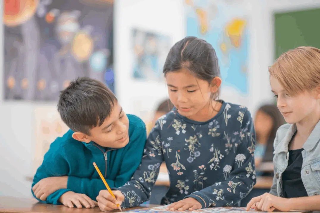 Tres niños colaboran en una actividad escolar en un aula llena de color y aprendizaje. Imagen educativa que refleja trabajo en equipo, creatividad y educación inclusiva. Ideal para contenido sobre métodos de enseñanza, colaboración entre estudiantes y desarrollo infantil en entornos educativos modernos y motivadores.