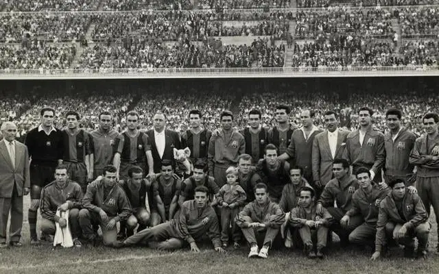 Fotografía histórica del FC Barcelona, capturada en un estadio lleno de aficionados apasionados. La imagen muestra a los jugadores y cuerpo técnico en un momento icónico de la historia del club. Perfecta para contenidos relacionados con la historia del Barça, sus leyendas, y el impacto del equipo en el fútbol mundial. Ideal para aficionados y proyectos sobre fútbol y cultura deportiva.