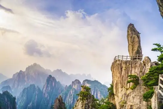 La imagen muestra un impresionante paisaje de las Montañas Amarillas (Huangshan), uno de los destinos naturales más icónicos de China. En la imagen se pueden observar las características formaciones rocosas, junto con pinos centenarios que crecen de manera singular entre los acantilados. Las Montañas Huangshan, famosas por sus picos escarpados, los mares de nubes y su espectacular belleza natural, han sido una fuente de inspiración para poetas, pintores y viajeros durante siglos. Este sitio es Patrimonio de la Humanidad por la UNESCO y es un destino imprescindible para los amantes del senderismo y los paisajes de montaña. La plataforma de observación en la cima brinda a los visitantes una vista impresionante y panorámica del entorno.