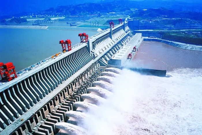 Presa de las Tres Gargantas en China - Ingeniería Hidroeléctrica en el Río Yangtsé  La imagen muestra la majestuosa Presa de las Tres Gargantas, la mayor planta hidroeléctrica del mundo situada en el río Yangtsé, en China. Esta obra de ingeniería monumental es un símbolo del avance tecnológico y la capacidad de infraestructura de China. La presa, conocida por su impacto tanto en la producción de energía renovable como en el control de inundaciones, es capaz de generar enormes cantidades de electricidad que abastecen a millones de personas en el país. Esta imagen resalta las características principales de la estructura, con agua fluyendo a través de sus compuertas y mostrando la magnitud y eficiencia de la presa en la gestión de recursos hídricos.